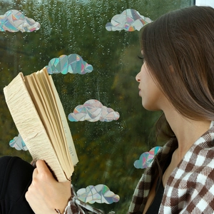 Rainbow prism cloud window stickers on glass with a person reading by a rainy window