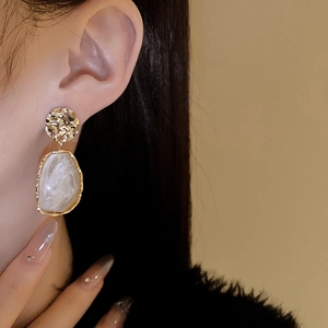 Close-up of vintage irregular golden earrings with white marble pattern on a model
