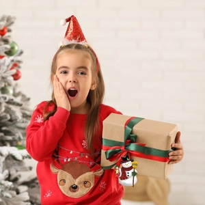 Close-up of a festive snowman ornament on a gift box held by a girl near a Christmas tree
