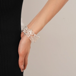 Detail eines silbernen Armreifens mit Blumenmuster am Handgelenk vor schwarzem Strick