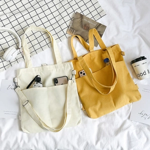 Detail view of large canvas tote bags with front pockets in beige and ginger yellow