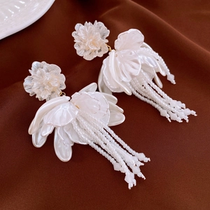 Macro view of white floral earrings with long bead tassels on dark fabric background