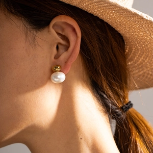 Elegant gold bead and large pearl drop earrings on a model with sunset shadow effects