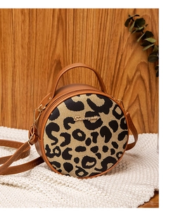 Close-up of circular leopard print handbag with brown leather trim and golden logo