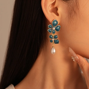 Close-up of blue enamel flower earrings with pearl accents and waterdrop pendant on model