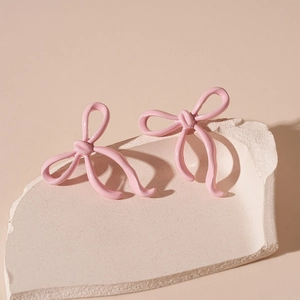 Close-up of pink lacquered bow stud earrings on a minimalist decorative stone base