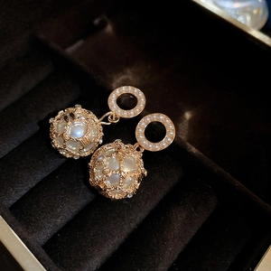 Close-up of golden grid cage earrings with pearls on black velvet jewelry box