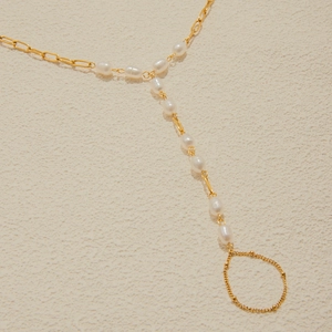 Dettaglio del bracciale da mano in acciaio dorato con perle d'acqua dolce e anello