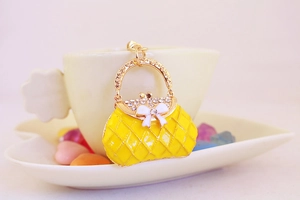 Detail of yellow enamel handbag keychain with rhinestones and white bow on a cup