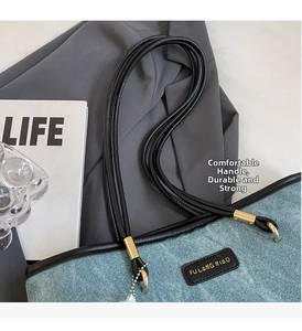 Detail of light blue denim tote bag with black leather trim and gold metal hardware