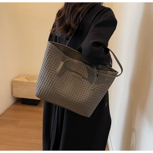 Detailed view of large dark grey woven texture tote bag worn by a model in a room