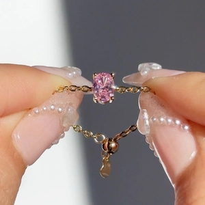 Macro detail of adjustable gold chain ring featuring a pink oval zircon stone and heart charm