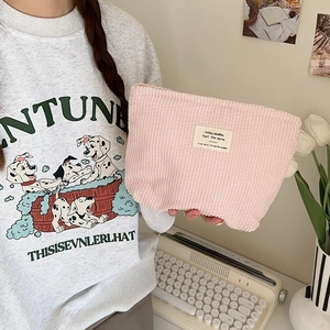 Pink corduroy makeup pouch with fabric label being held in a cozy home office setting