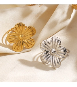 Détail de bagues fleurs en or et argent sur satin beige avec une finition métallique polie