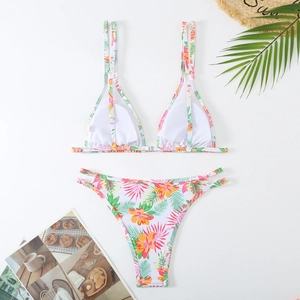 Flat lay of tropical floral bikini set with orange flowers and green palm leaves