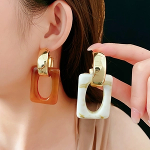 Detail of geometric C-shaped earrings with amber resin and marble texture finish