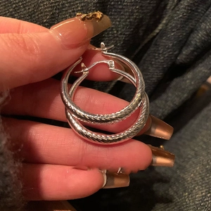 Gros plan détaillé de boucles d'oreilles créoles argentées torsadées tenues à la main