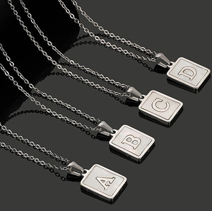 Macro shot of silver rectangular shell necklaces featuring engraved letters A B C and D