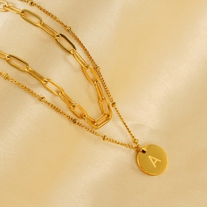 Close-up of gold double-layer necklace with paperclip chain, bead chain and letter A pendant