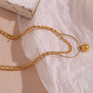Detail of double-layer gold necklace featuring small beads and a round sphere pendant