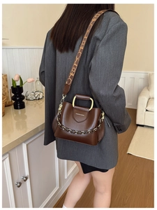 Detail view of brown PU leather bucket bag with gold handle and printed strap on model