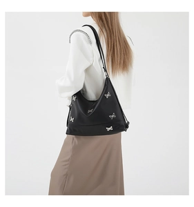 Model wearing a black PU shoulder bag with silver butterfly charms on white background