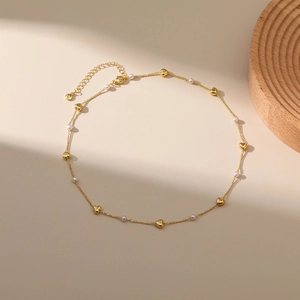 Detail von goldenen Herzperlen und weißen Perlen an einer minimalistischen Halskette