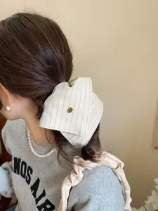 Detail of a vintage striped cream scrunchie with a gold metal button worn on a ponytail