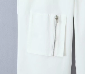 Detail of white cargo pants featuring a large pocket with a silver metal zipper