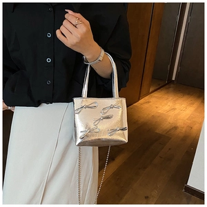 Detail of silver metallic handbag with 3D bow decorations and fine metal chain strap