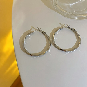 Macro detail of large twisted silver hoop earrings with elegant metallic texture