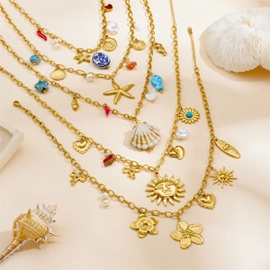 Detail of layered gold necklaces with shell, starfish and sun charms on sand background