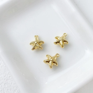 Detailed view of three 14k gold-plated starfish charms on a white ceramic plate