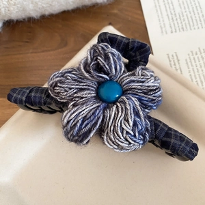 Detail of grey-blue knitted flower hair claw clip with dark blue bead on a plaid base
