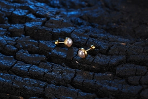 Macro shot of gold pearl stud earrings on a natural textured dark wood background