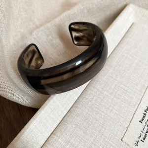 Close-up of dark brown marble acrylic open bangle on neutral linen and book