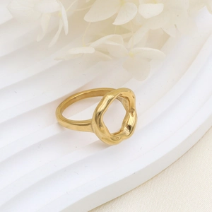 Détail d'une bague géométrique dorée sur surface texturée blanche avec fleurs séchées