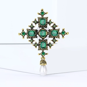 Macro detail of Baroque bronze cross brooch with green gems and white teardrop pearl