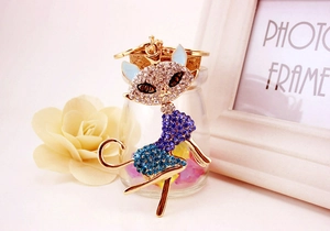 Detail of a golden cat keychain with blue and clear rhinestones next to a yellow rose