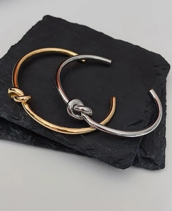 Detail shot of stackable gold and silver knot bangles on a black stone coaster