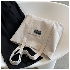Detail of off-white canvas tote bag with black fashion label on a white chair