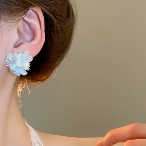 Detail view of light blue resin flower stud earrings worn on ear with soft lighting