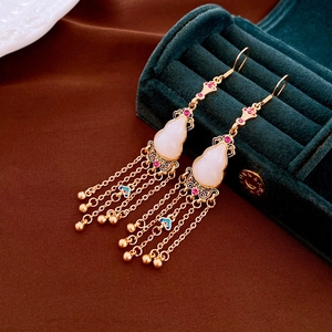 Detail of gold-plated gourd earrings with tassels on a dark green velvet jewelry box