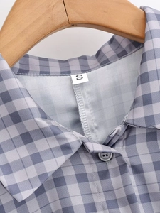 Dettaglio del colletto di camicia a quadri grigio-viola con etichetta S e bottone in resina
