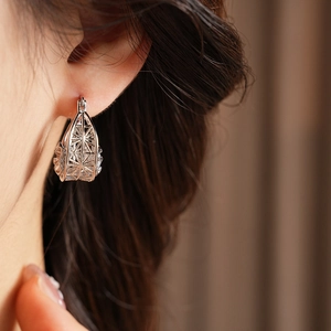 Close-up of a silver hollow geometric flower earring worn on an ear with soft lighting