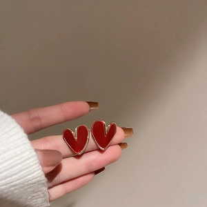 Close-up of red heart earrings with gold trim held by hand against yellow background