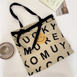 Flat lay of large canvas tote bag with black letter print and yellow smiley face detail