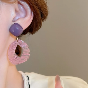 Close-up of geometric resin drop earrings in purple and pink tones on female model