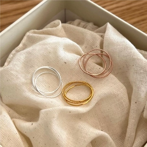 Three-color twisted rope stackable rings in silver, gold, and rose gold on white fabric
