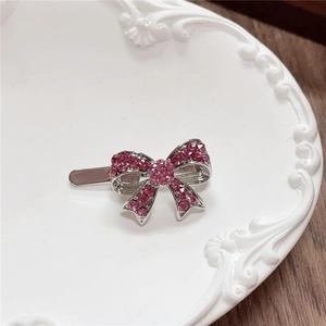 Detail of silver bow hair clip with pink rhinestones on a white ceramic plate